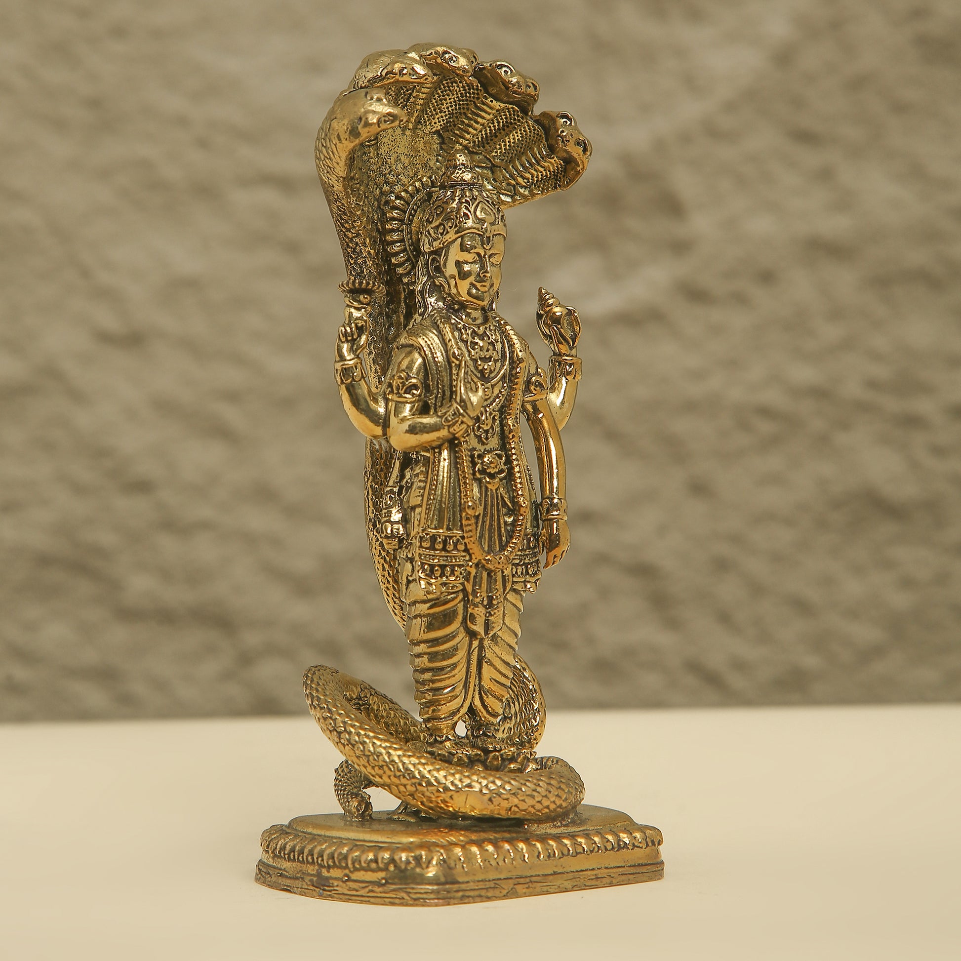 Gold-colored statue of a deity with a snake on a textured background