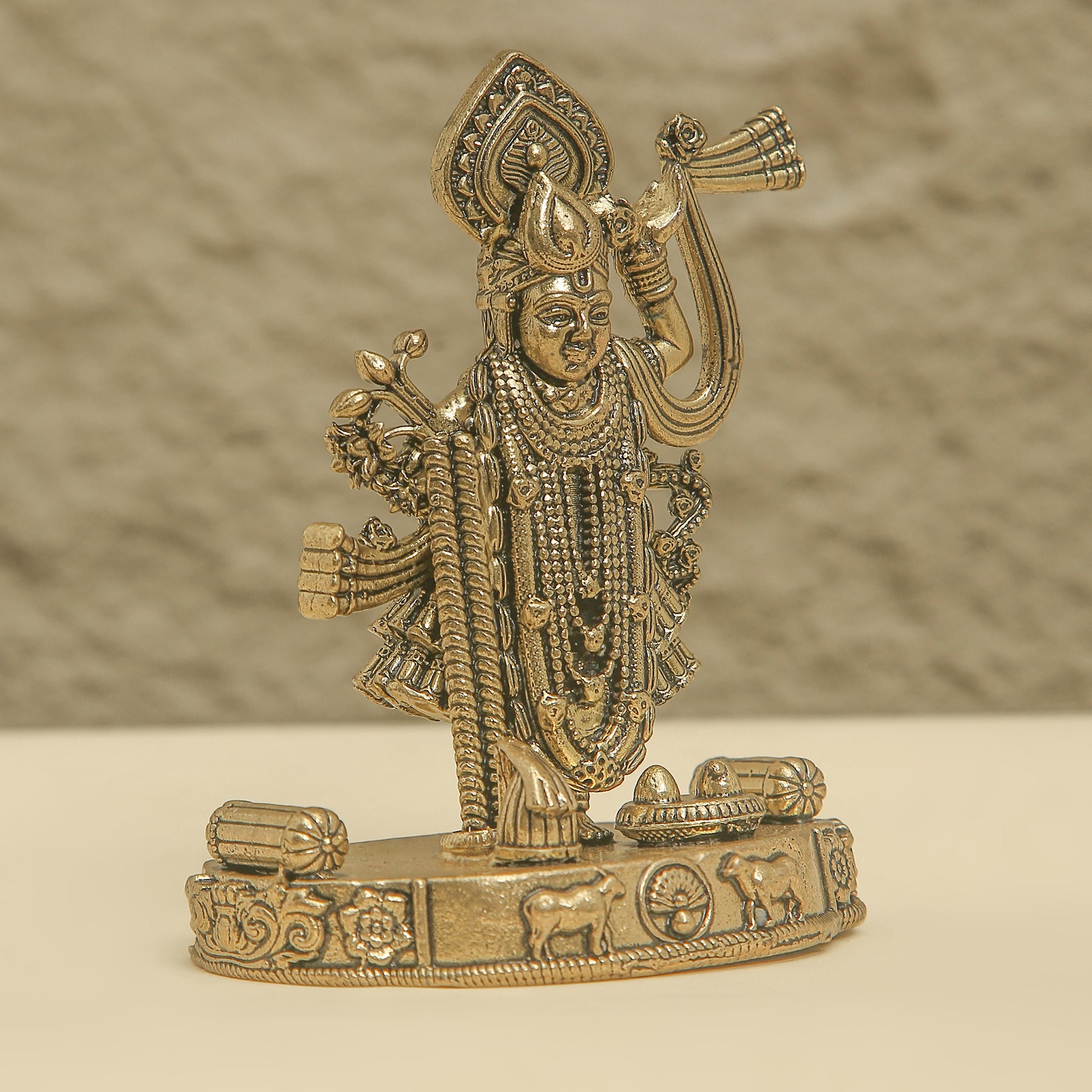 Gold-colored statue of a deity on a beige surface with a neutral background