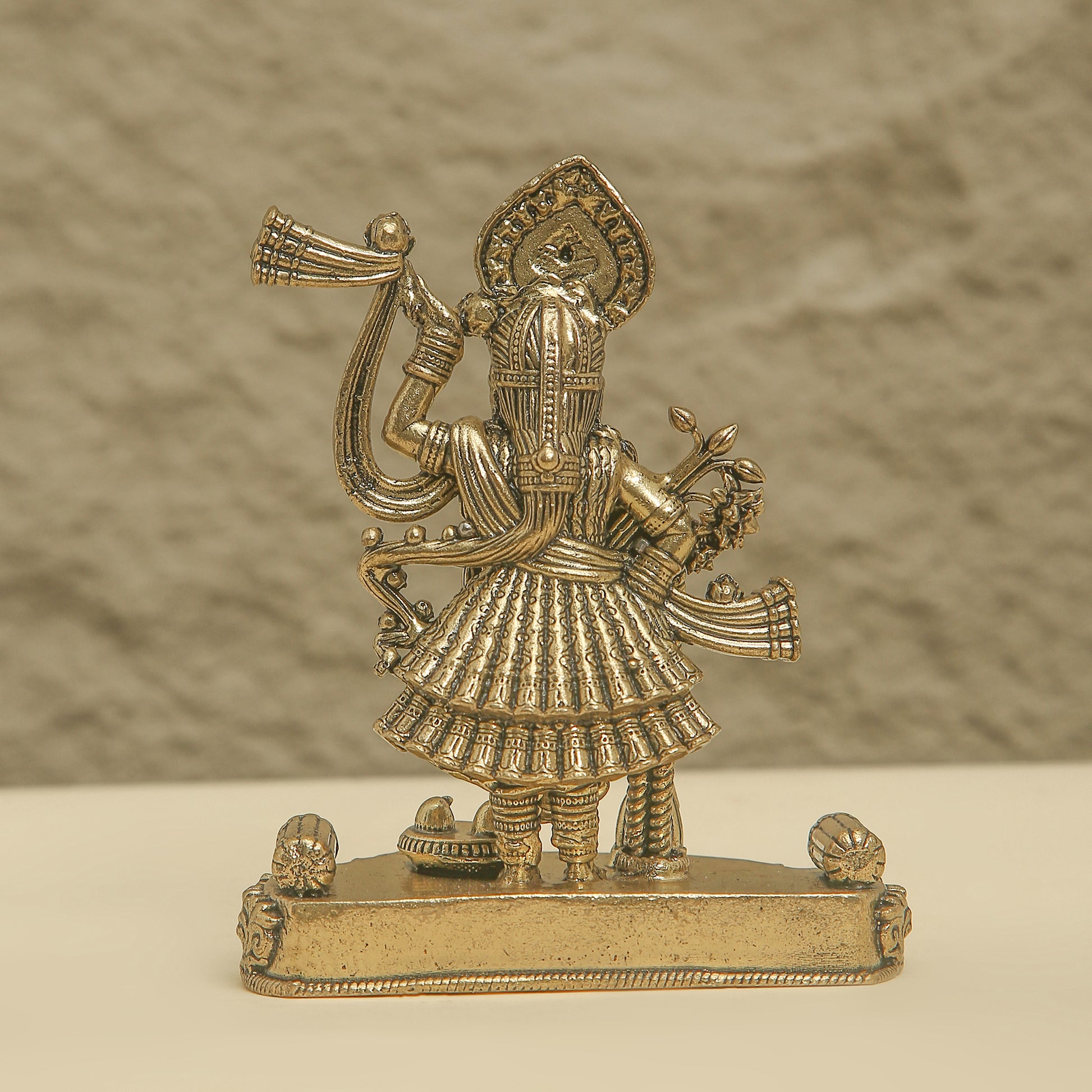 Gold-colored figurine of a deity on a textured beige background