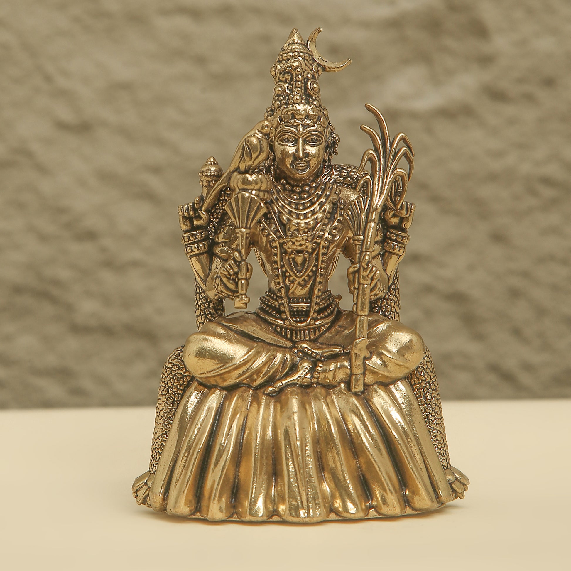 Gold-colored statue of a seated figure with intricate details on a neutral background