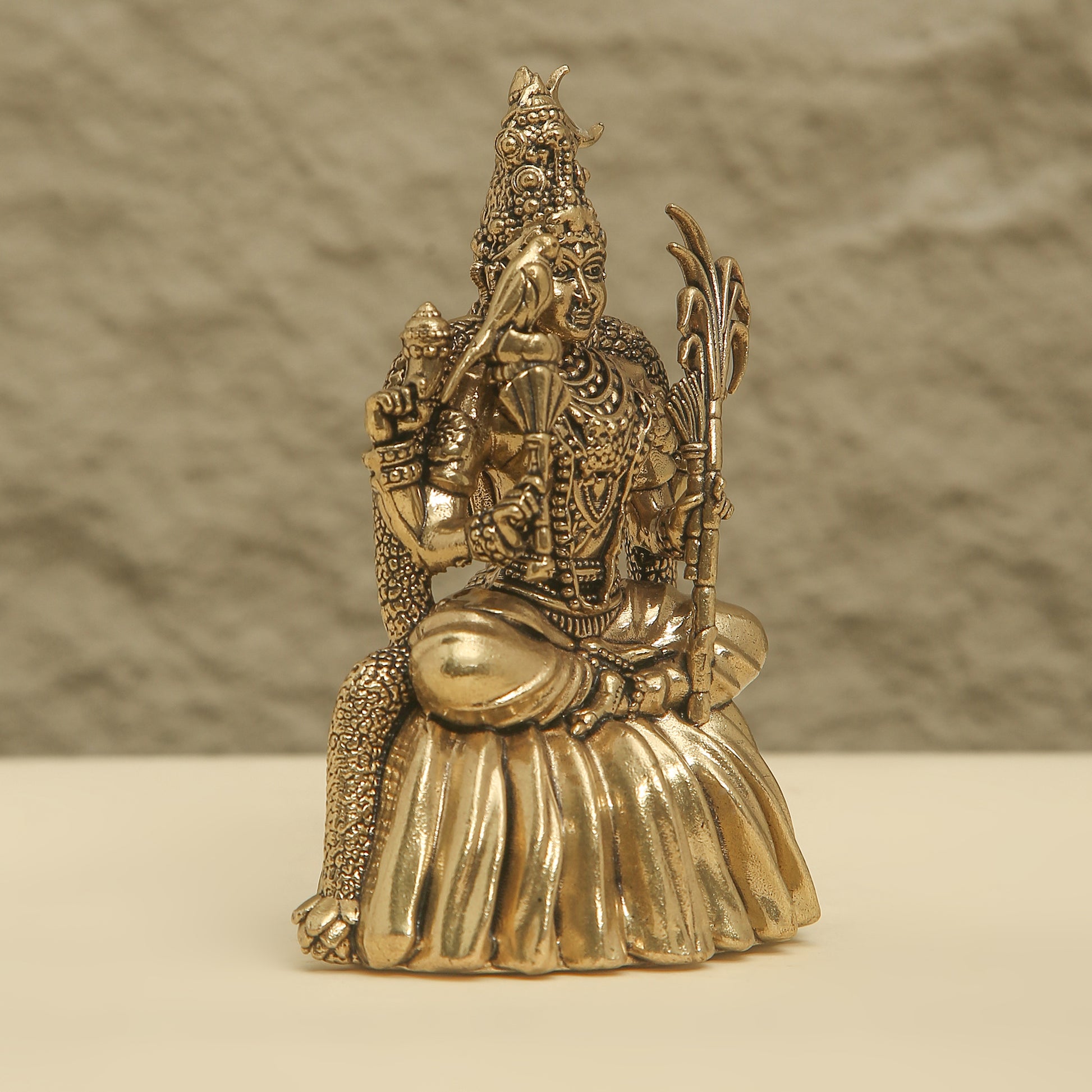 Bronze statue of a seated figure with intricate detailing on a beige surface and brown background