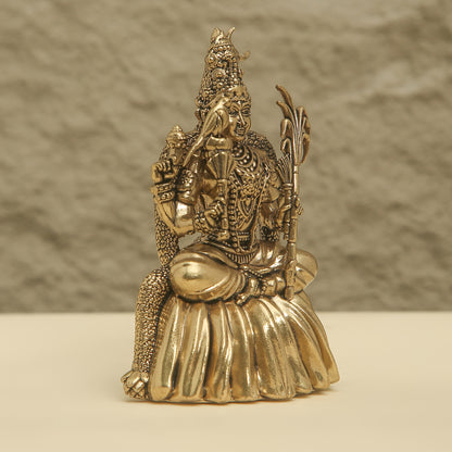 Bronze statue of a seated figure with intricate detailing on a beige surface and brown background