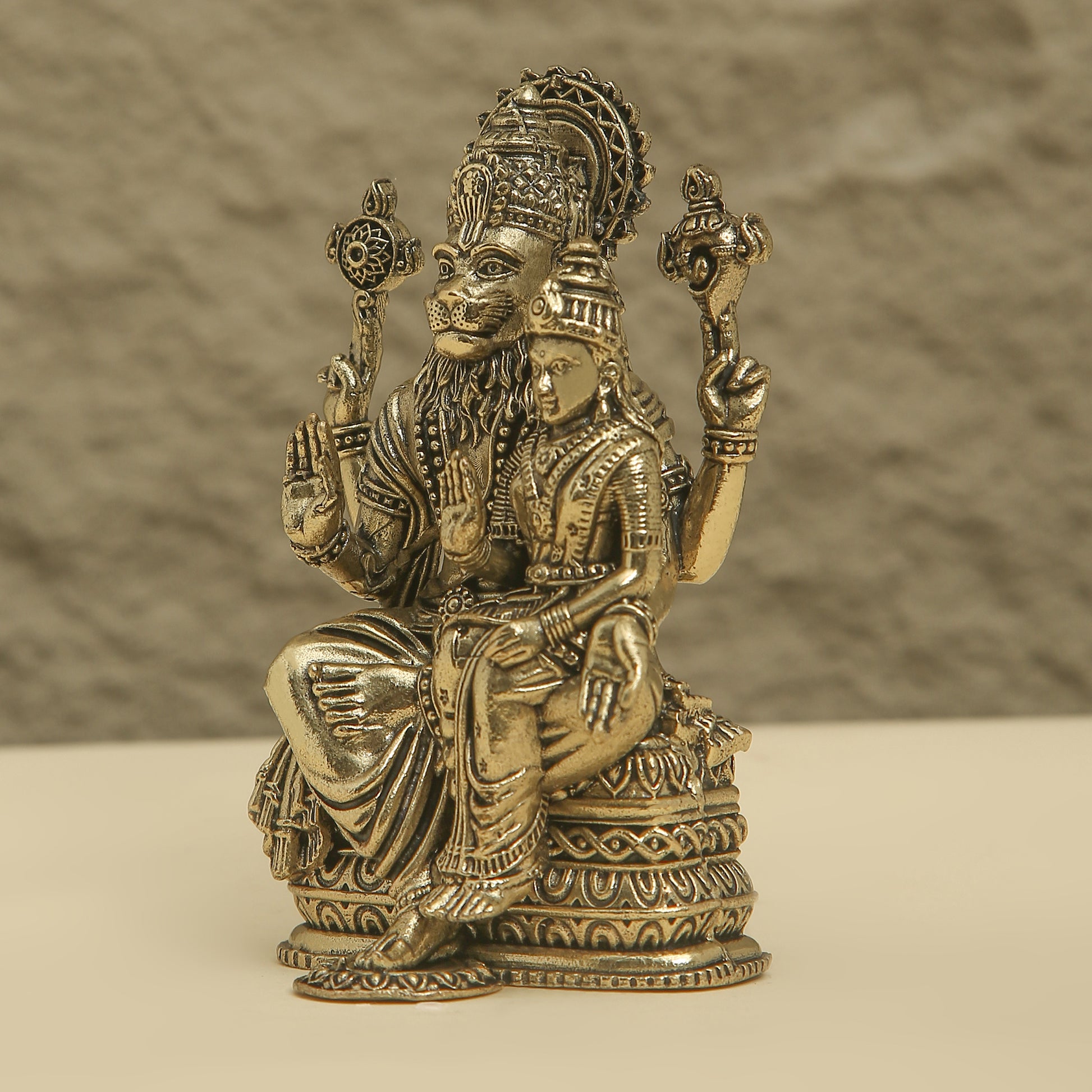Bronze statue of a seated figure with intricate details on a beige background