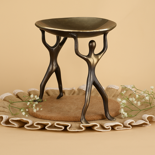 Bronze sculpture of two figures holding a round table on a beige background