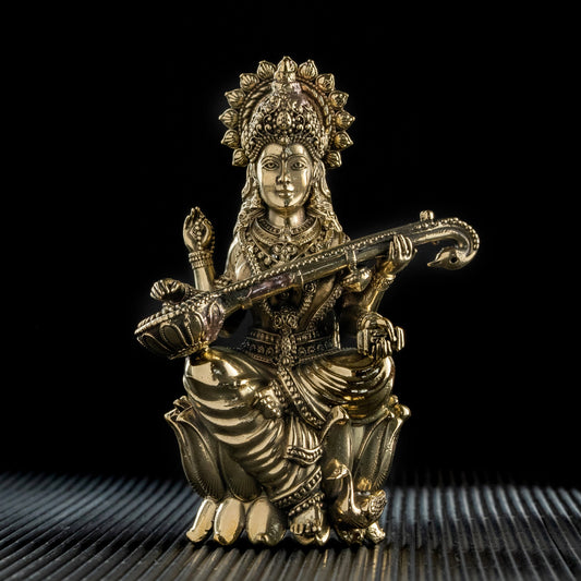 Gold-colored figurine of a seated figure playing a stringed instrument on a textured surface with a black background