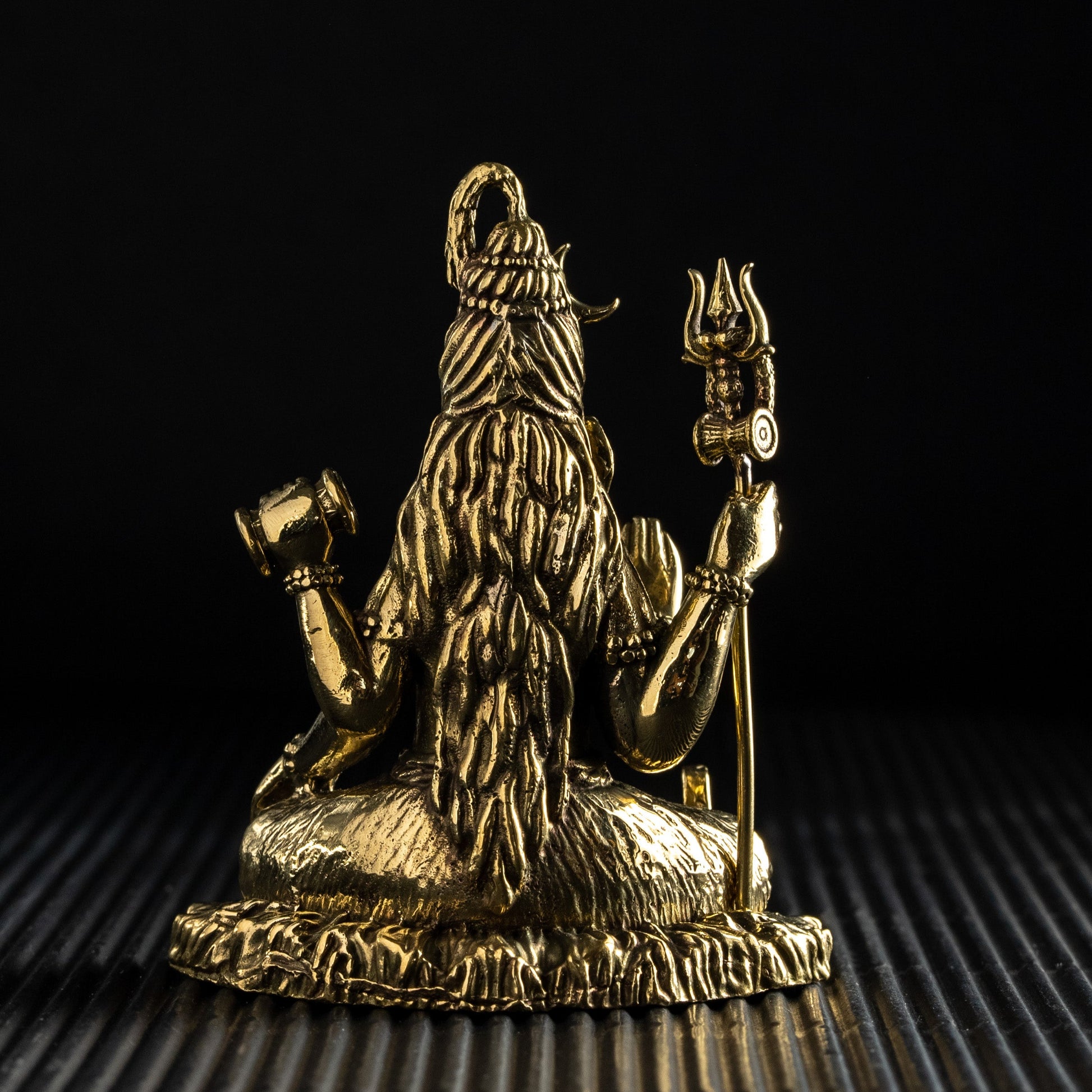 Gold-colored statue of a deity on a textured surface with a black background