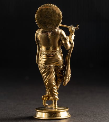 Gold statue of a deity holding a flute on a dark background