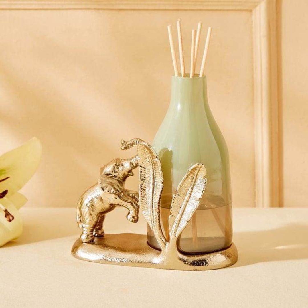 Decorative bottle with gold elephant and leaf design on a beige surface