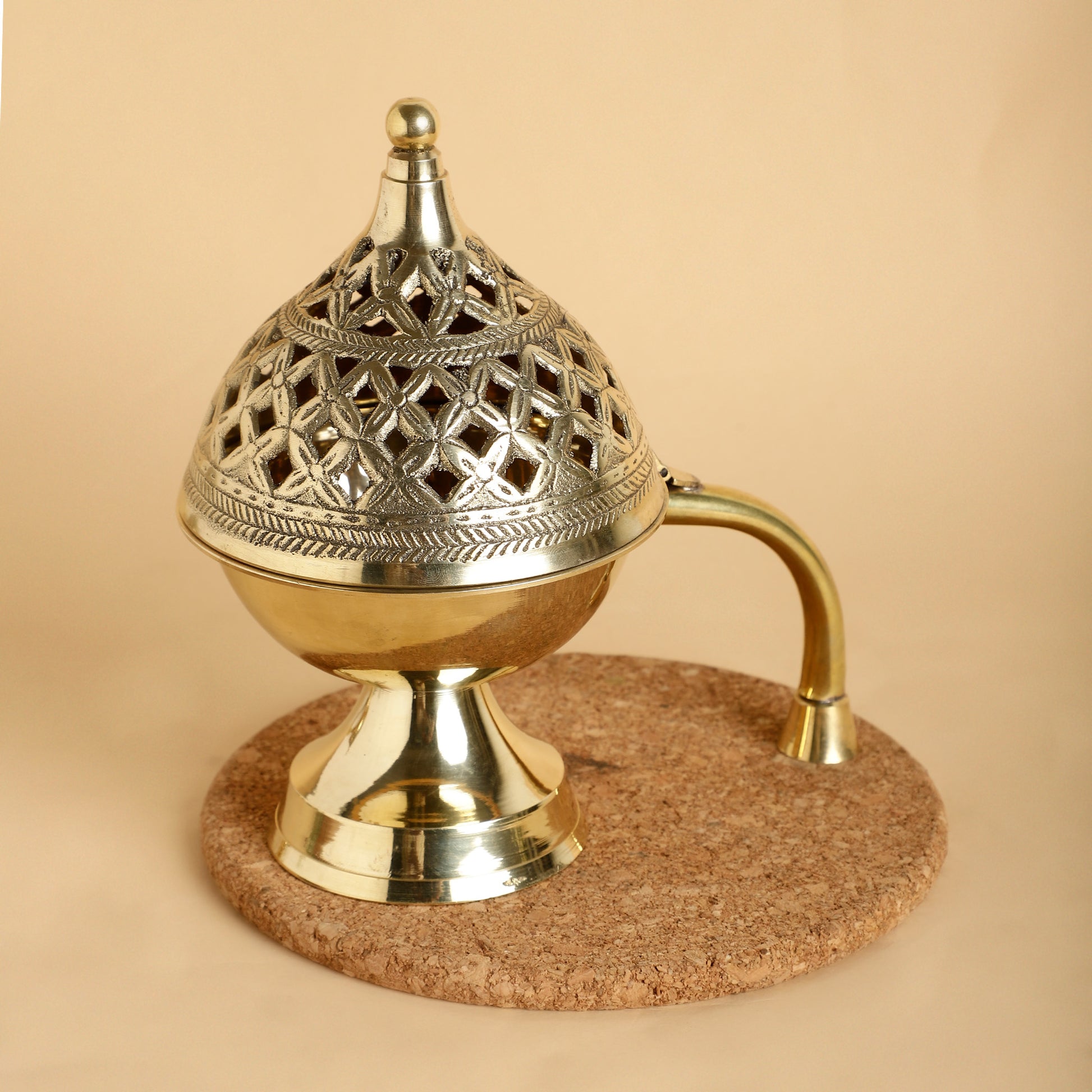Decorative brass incense burner on a cork base against a beige background