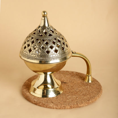 Decorative brass incense burner on a cork base against a beige background