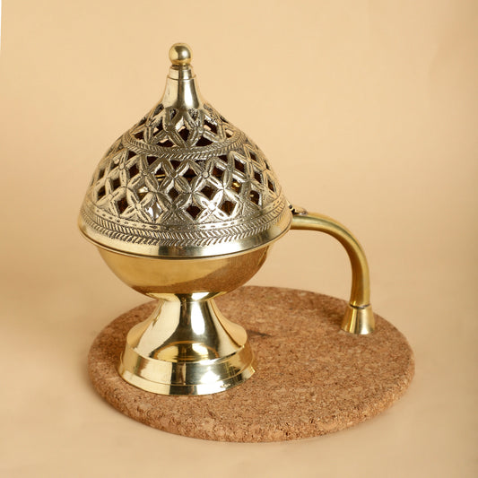 Decorative brass incense burner on a cork base against a beige background