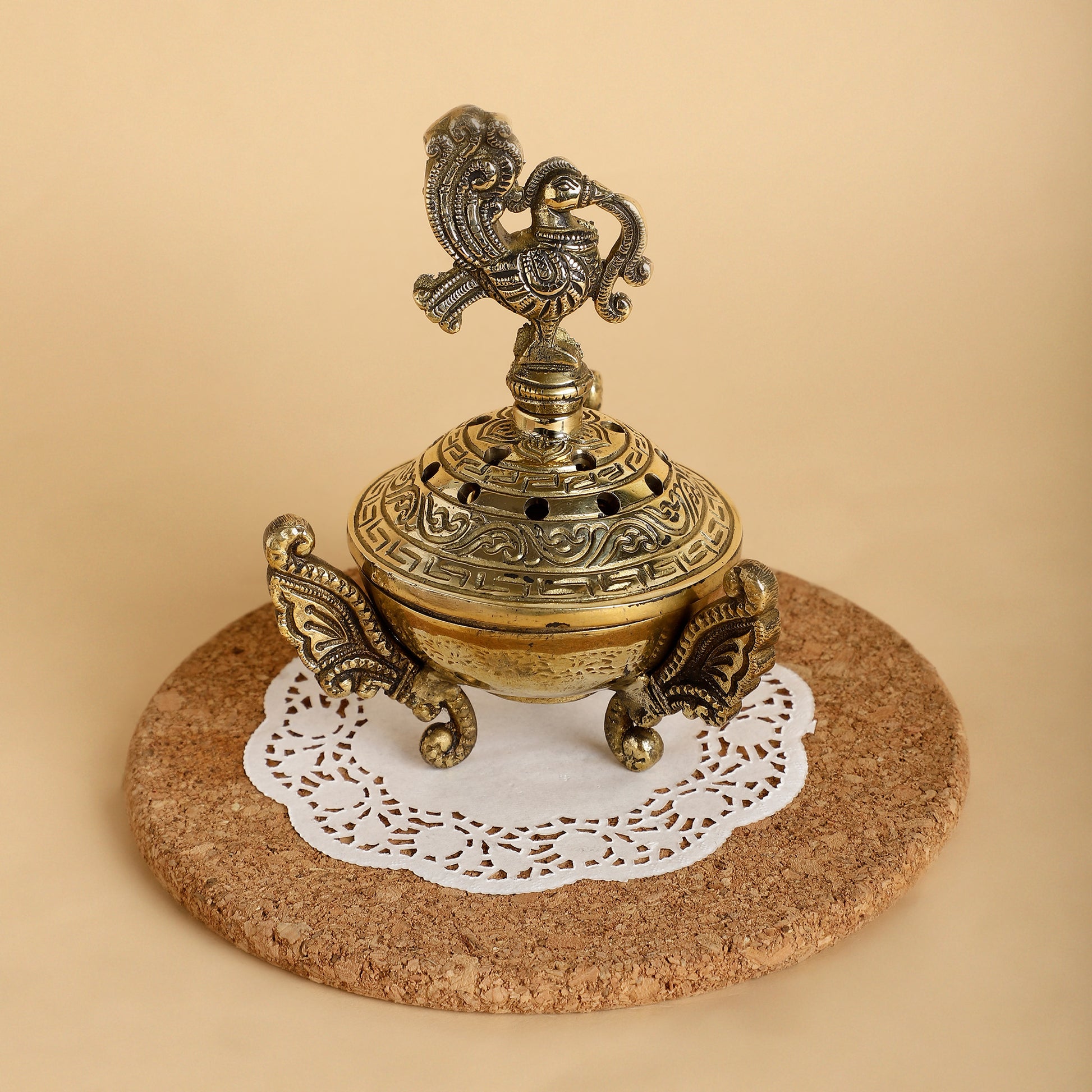Decorative brass incense burner on a cork coaster with a white doily underneath