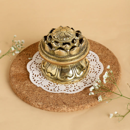 Decorative brass incense burner on a cork coaster with white doily and small flowers.