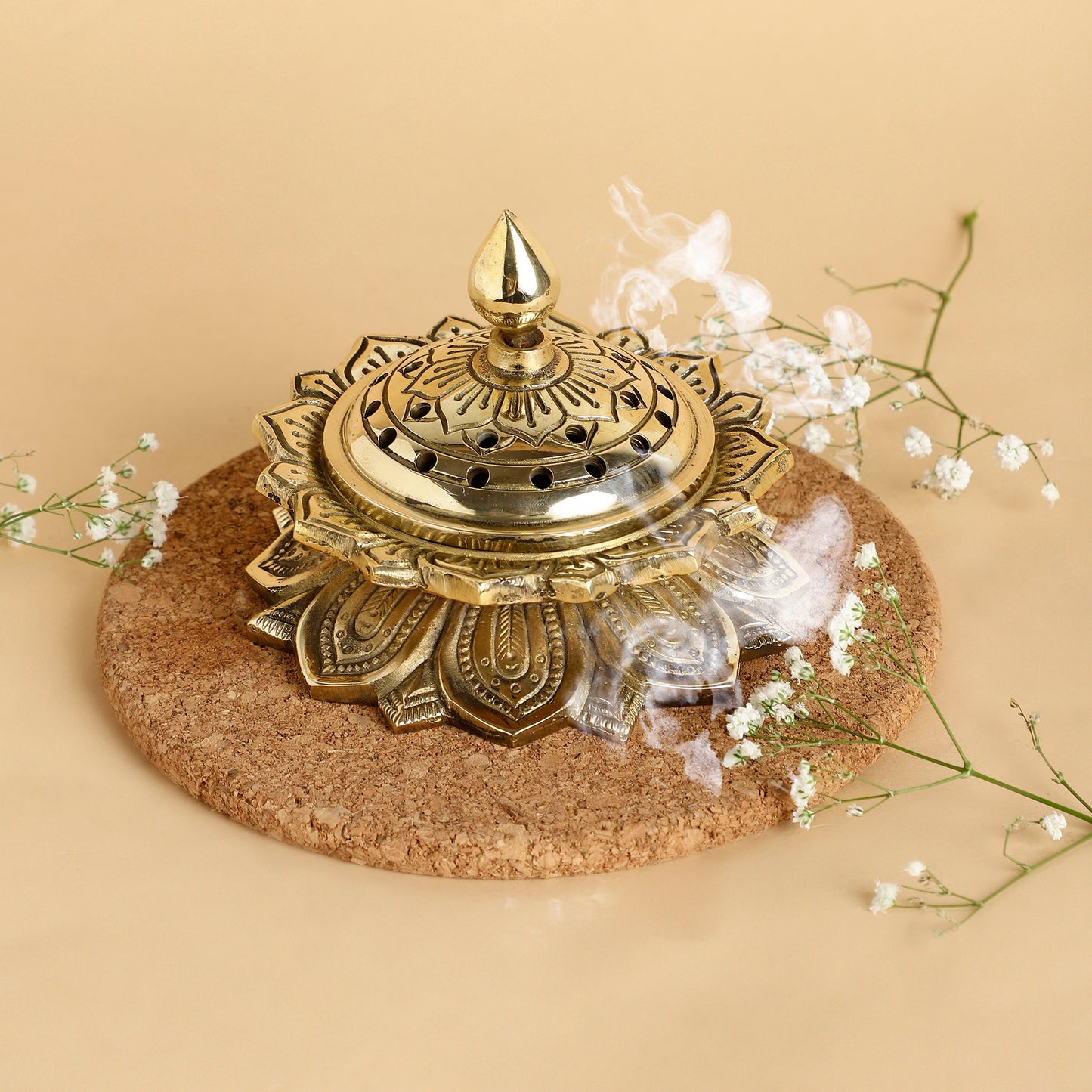Decorative gold incense burner on a cork base with smoke and flowers on a beige background