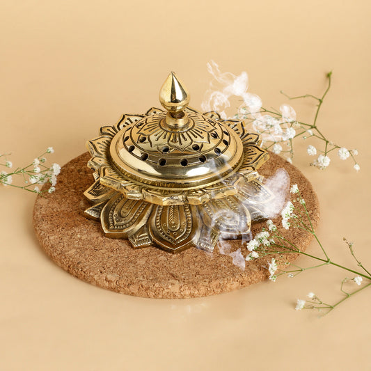 Decorative gold incense burner on a cork base with smoke and flowers on a beige background