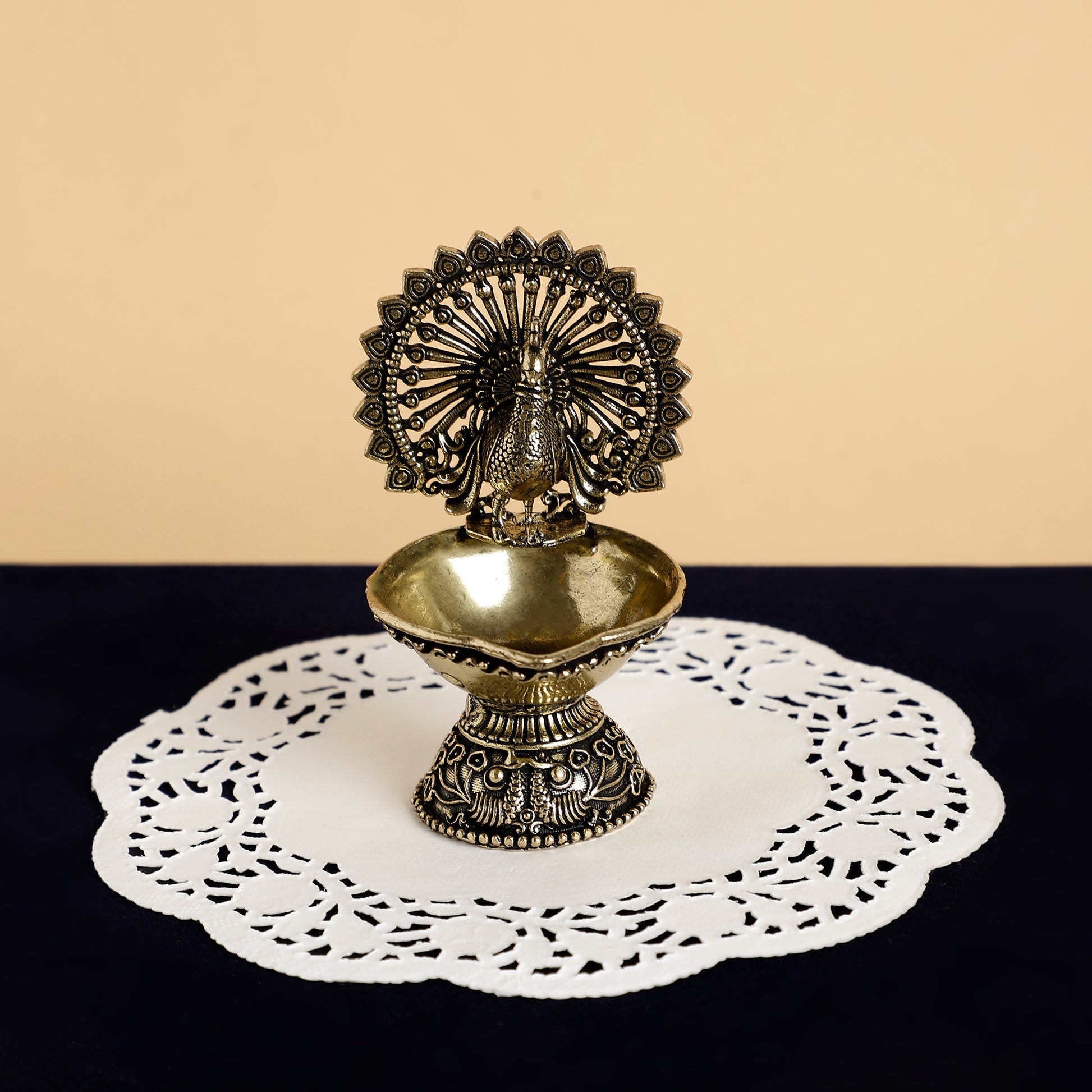 Decorative metal oil lamp on a doily with a beige and black background