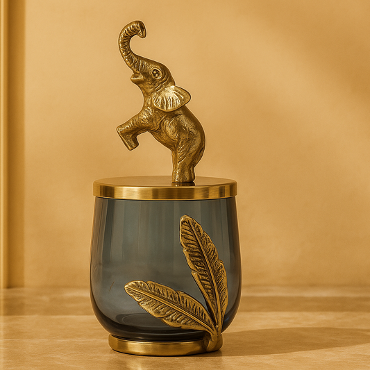 Decorative object with a gold elephant on top of a dark glass container with gold leaf design, against a beige background.
