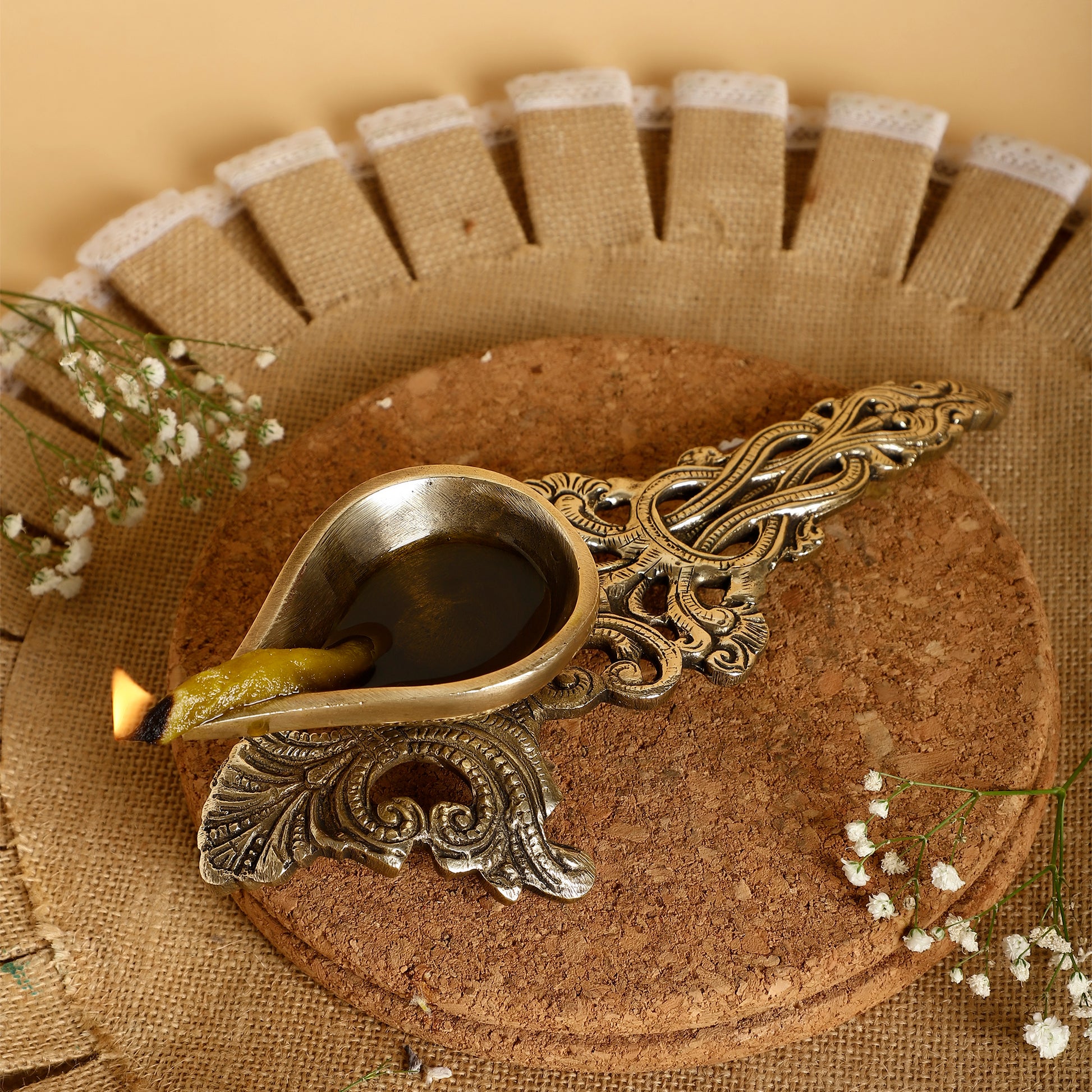 Decorative oil lamp with intricate design on a textured surface with flowers.
