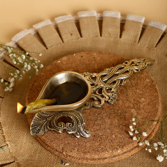 Decorative oil lamp with intricate design on a textured surface with flowers.