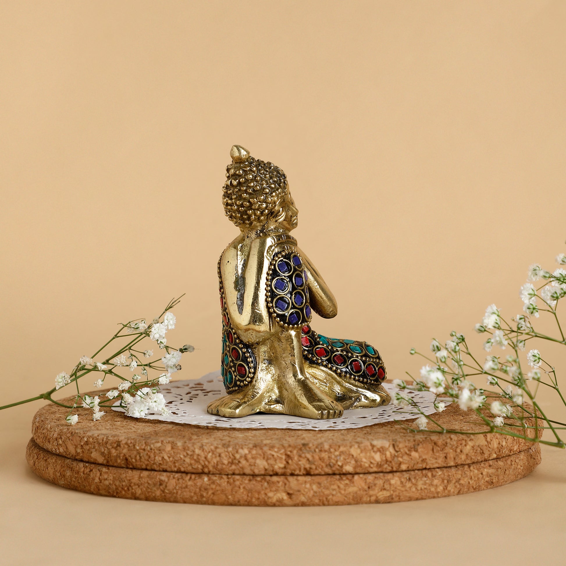 Decorative statue of a seated figure with gemstone details on a cork base with flowers.