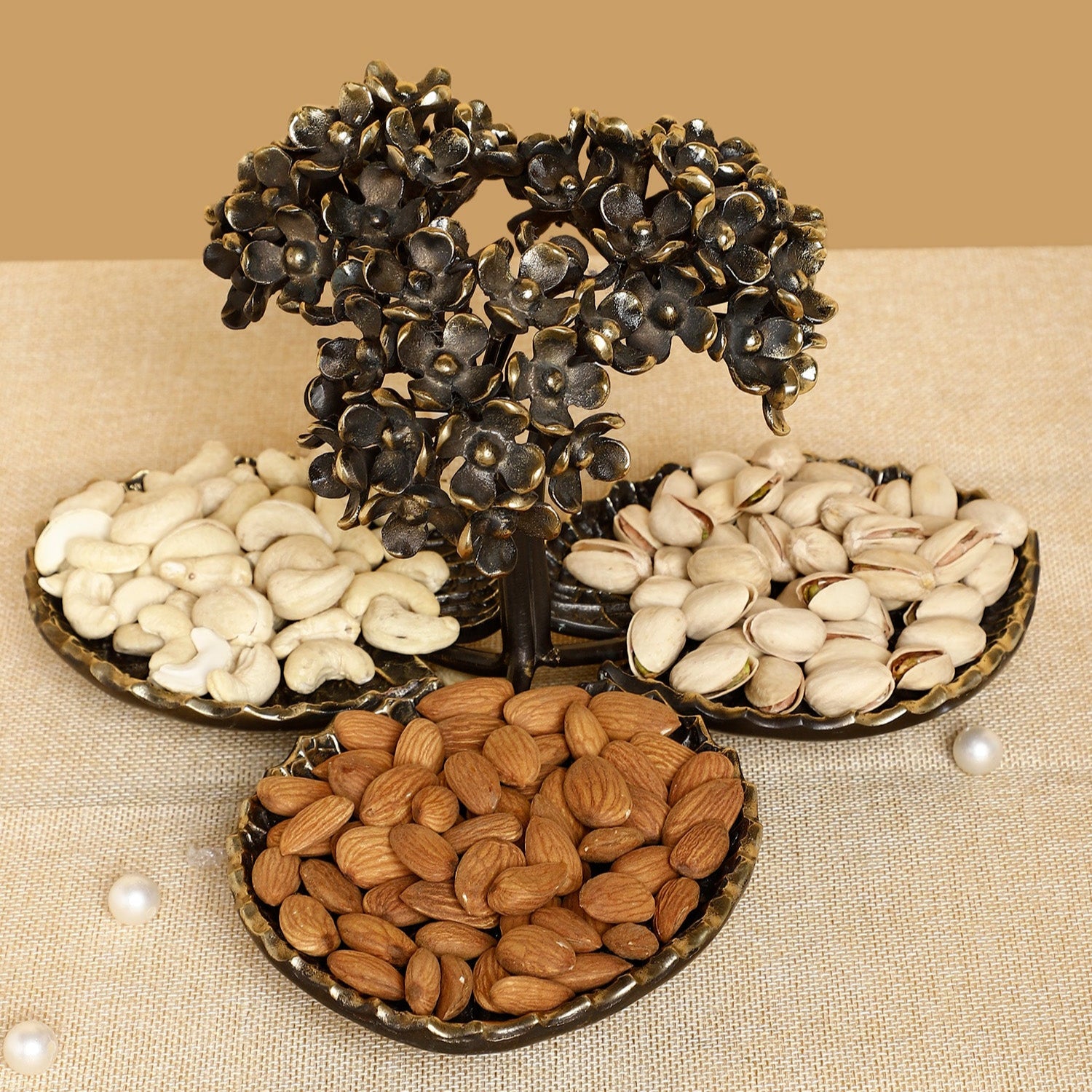 Decorative metal tree with three trays of nuts on a beige background