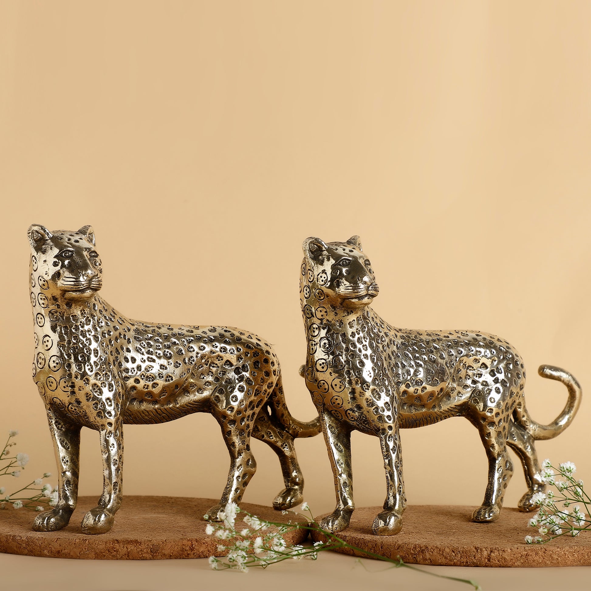 Two metallic leopard sculptures on a beige background
